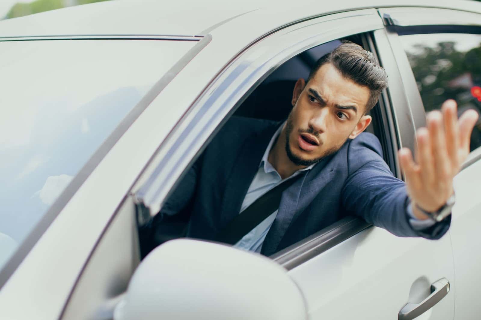 A man in a suit driving a car and waving his hand